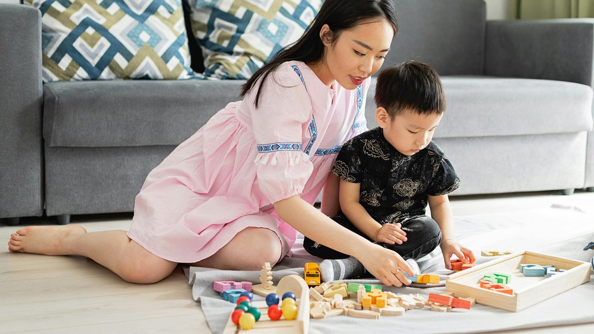 A mother and her young son sit together on the floor at home doing an alphabet and shape sorting activity